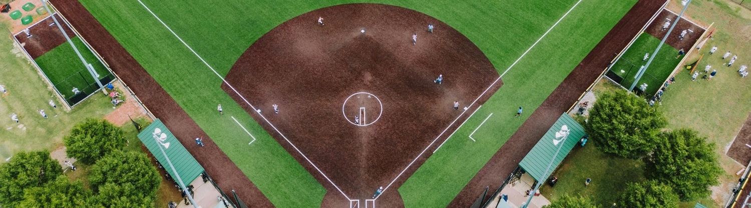 birds eye view of a synthetic baseball field with players on base. Brown artifcial grass for the infield and green artificial grass for the outfield.