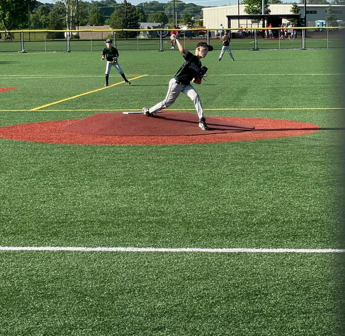 baseball pitcher throwing a pitch off an synthetic turf, removable mound. Red turf mound with green artificial turf for the infield and outfield