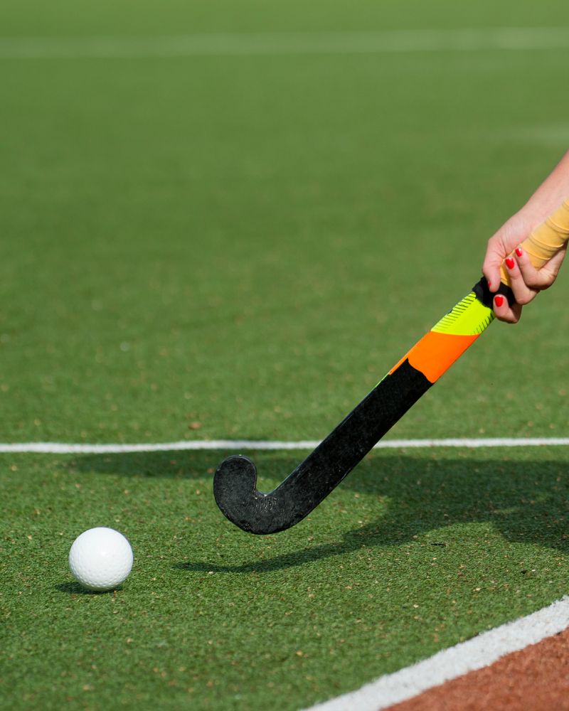 close up of a field hockey player with stick about to hit the hockey ball. Playing on an artificial turf hockey field with both red and green turf, and white lines