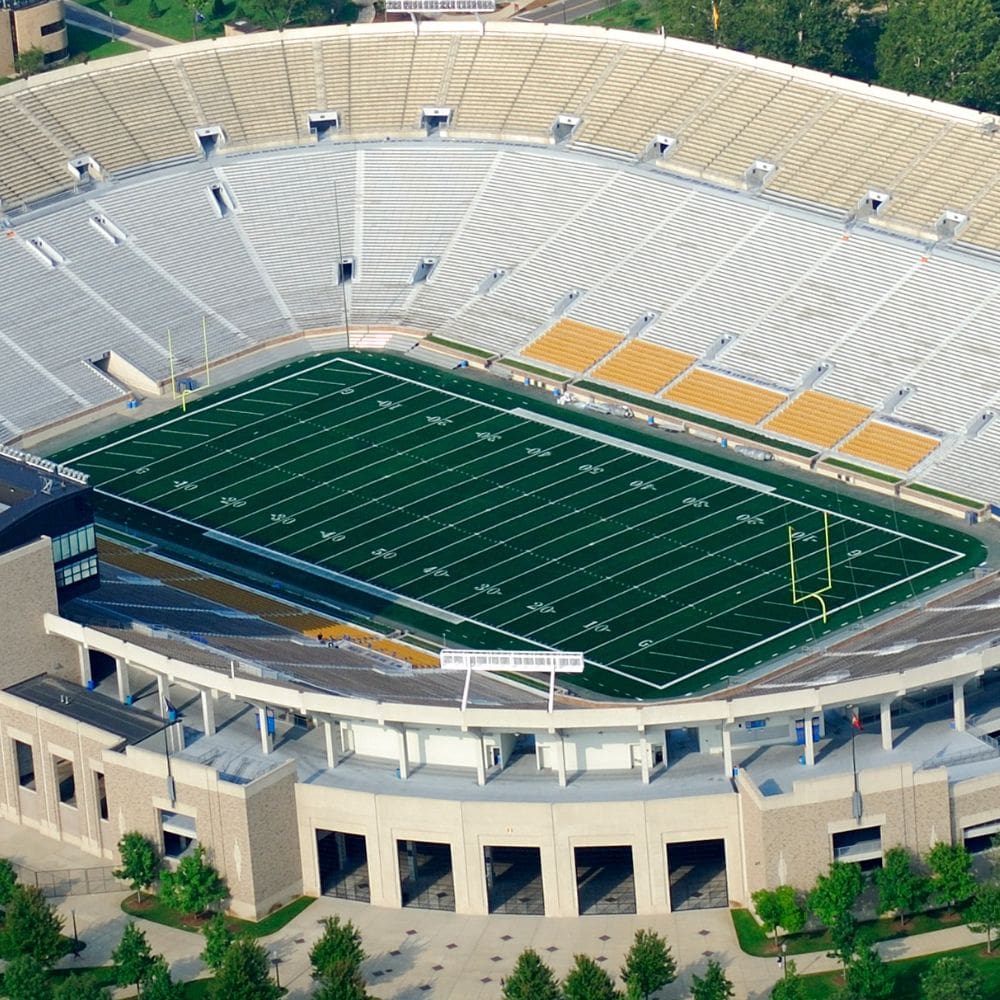 football stadium view from above. Shows a large grand stand and freshly installed synthetic athletic turf for football fields in the center of the stadium. Turf install done by Coyote Sports Turf